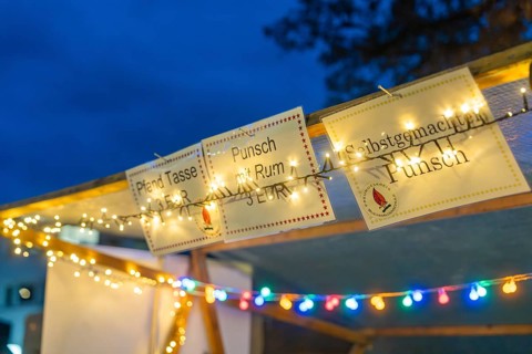 Glowing signs and fairy lights draw attention to a punch stand in the evening, Aidlingen Christmas