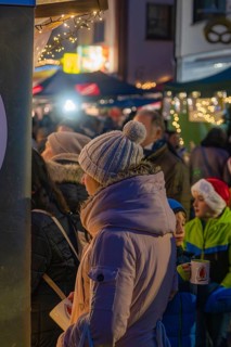 Woman in warm winter clothes holding coffee cup surrounded by children and twinkling lights at the