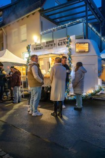 Friends chatting in front of an illuminated beverage stand at night, Aidlingen Christmas Market,