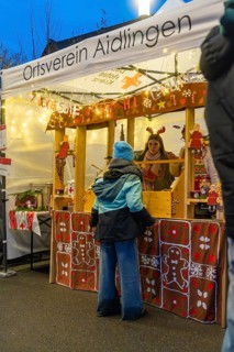 Christmas market stand with glowing decorations and people in front of it, Aidlingen Christmas