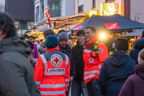 Red Cross members in uniforms happily interact at a well-attended Christmas market, Aidlingen