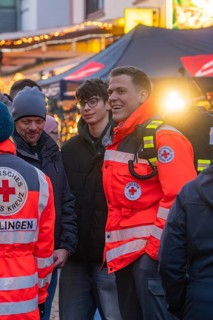 Red Cross paramedics stand at a Christmas market, engaged and friendly amidst the crowd, Aidlingen