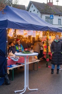 People stand at a decorated market stand under a tent at a busy Christmas market, Aidlingen