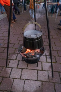 A cauldron hangs over a glowing fire on outdoor cobblestones at a Christmas market, Aidlingen