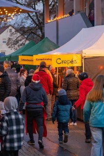 Visitors stroll along illuminated stands at an evening market, Aidlingen Christmas Market,
