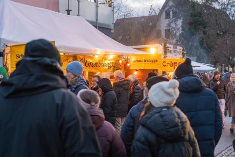 People wearing winter clothes in front of illuminated food stalls at a market, Aidlingen Christmas