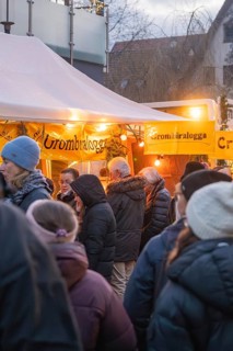 People stand at a brightly lit stand at a Christmas market, wrapped in warm clothes, Aidlingen