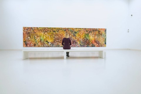 Woman sitting on bench looking at large, colorful, abstract work of art, Open Horizons exhibition,