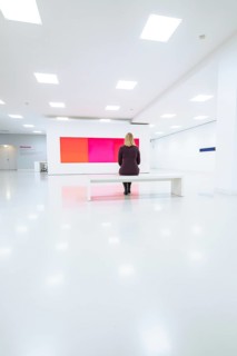 White minimalistic room with woman on a bench in front of colored painting, Open Horizons