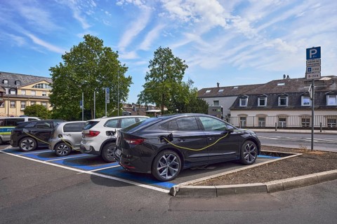 Parking lot, electric car, e-car with charging cable, general architecture, trees, blue sky,
