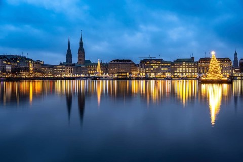The decorated and illuminated Alster fir tree on the Inner Alster with reflections on the water in
