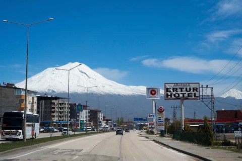 Road with passing vehicles flanked by a hotel and snow-capped mountains in the background, Great