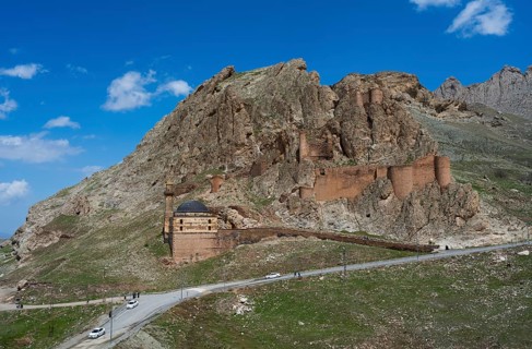 A mountain fortress with roads in the foreground surrounded by steep rocks under a bright blue sky,