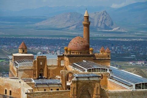 An ancient dome mosque in a mountainous landscape surrounded by a city under a blue sky, Ishak