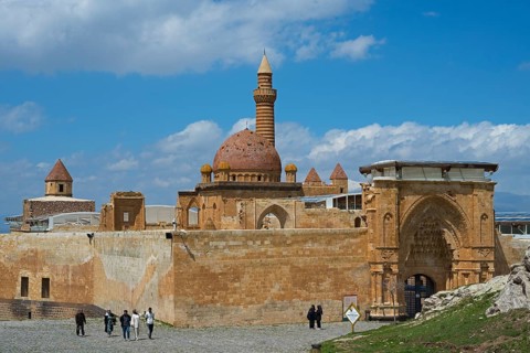 A historic building with a sandstone dome and minaret, surrounded by an old wall, under a blue sky,