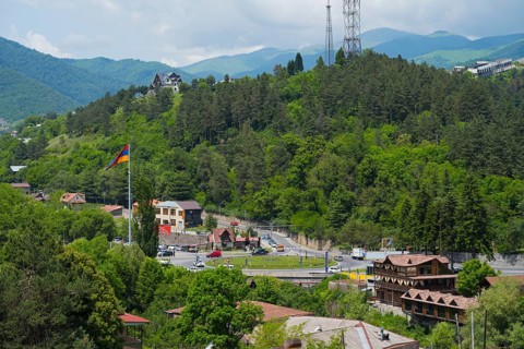 Panorama with mountains, forest, village, a flag and a road leading through the green landscape,
