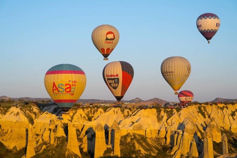 Balloons with logos floating over a rocky landscape with mountain views in the background, hot air