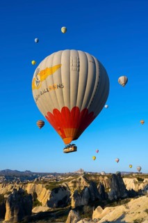 A large colorful balloon with decoration floats over a picturesque rocky landscape, hot air