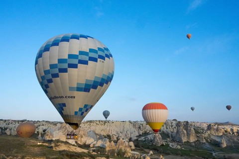 Hot air balloons of various colors float over a picturesque landscape and stand out against the