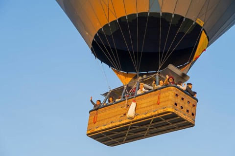 A hot-air balloon basket full of people floats in the warm morning light, symbolizing freedom and