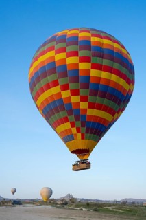 A colorful hot air balloon floats in daylight over a meadow under clear blue sky, Göreme National
