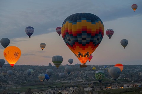 Colourfully patterned hot air balloons rise over the city and countryside of Cappadocia, Göreme