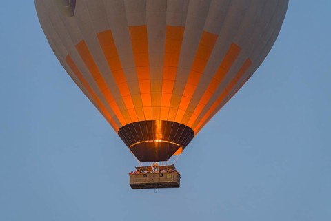Close-up of glowing hot air balloon with basket and flame against the morning sky, Göreme Tarihî
