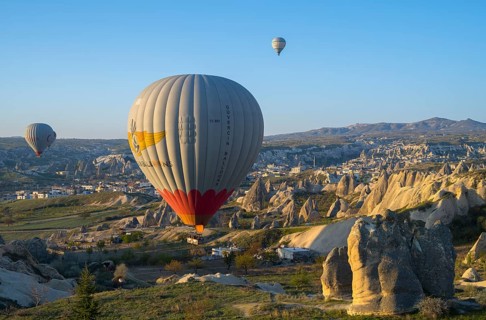Hot air balloons float over a rocky landscape at sunrise in Capadocia, Göreme National Park, Göreme
