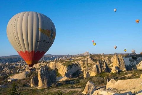 A large colorful hot air balloon moves elegantly over a rocky landscape, Göreme National Park,