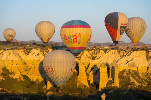 A group of balloons floats along a sunlit rock formation, hot air balloons, Göreme National Park,