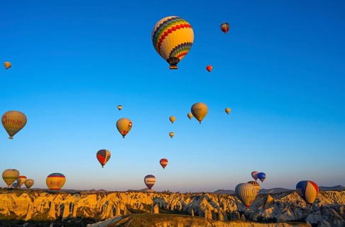 Hot air balloons float over rocks in a vast landscape in morning light, Göreme National Park,