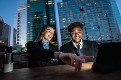 Diverse colleagues enjoying content on a digital tablet outdoors at night in an urban setting with