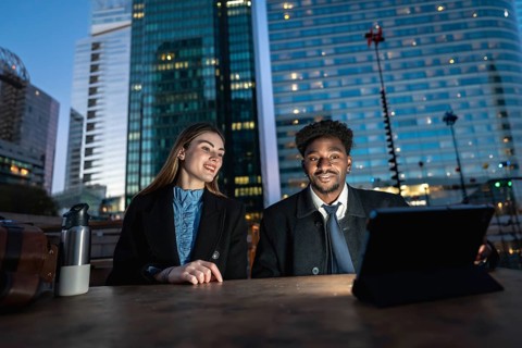Diverse business colleagues working together on a digital tablet outdoors on a wooden table,