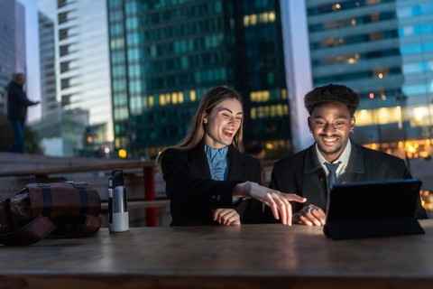 Two diverse business colleagues reviewing content on a digital tablet, discussing and laughing