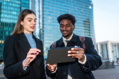 Two diverse business professionals collaborate outdoors in a modern city, smiling as they review