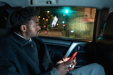 Afro american passenger riding in a car, looking out the window at city lights while holding a