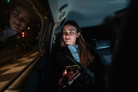 Young businesswoman commuting by car at night, sitting in backseat and looking out the window while