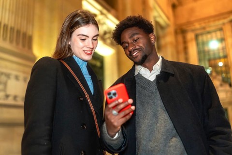 Diverse couple standing close, looking at a smartphone screen and smiling, enjoying connecting and