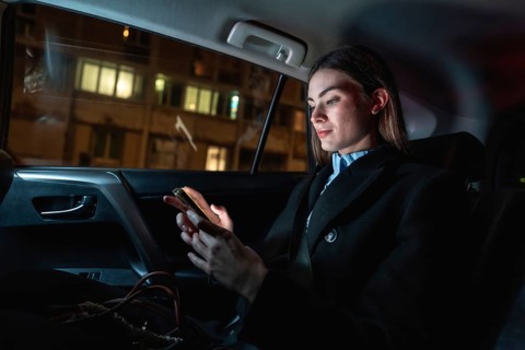 Young businesswoman commuting by car at night, focused on her smartphone as she scrolls messages
