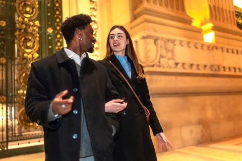 Smiling interracial couple enjoying a romantic night out, walking closely and conversing in front