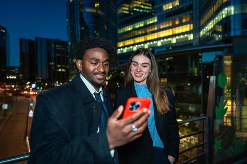 Diverse business colleagues reviewing content on a smartphone, standing outdoors at night with