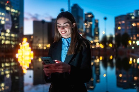 Young professional woman smiling happily while interacting with her mobile phone against a blurred
