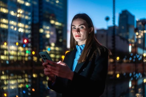 Young businesswoman looking at camera while holding a mobile phone in her hands and texting,