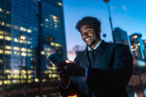 Young black man connecting with his smartphone, illuminated by the screen's glow, against a blurred