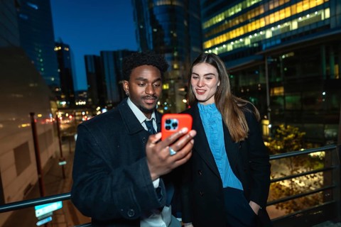 Diverse business professionals standing outside in a city at night, sharing content on a
