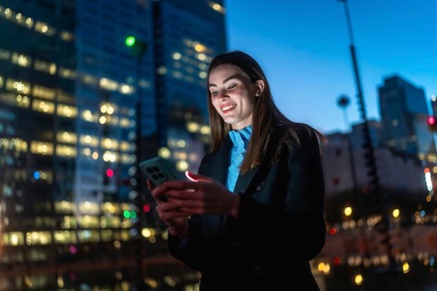 Woman smiling illuminated by smartphone screen, connecting and enjoying digital content outdoors in