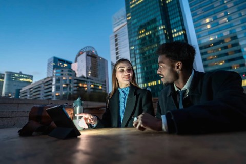Two diverse business colleagues discussing ideas and working together on a digital tablet at night,