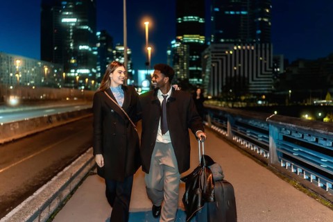 Diverse couple walking together holding hands and pulling a suitcase in a modern urban city