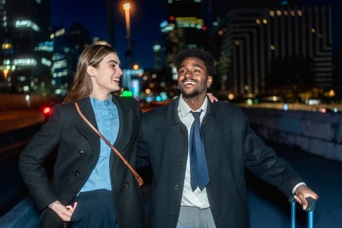 Diverse business colleagues smiling and walking together carrying luggage in an urban setting at