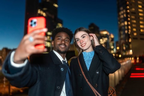Diverse couple happily capturing a moment together using a mobile device for a selfie, illuminated